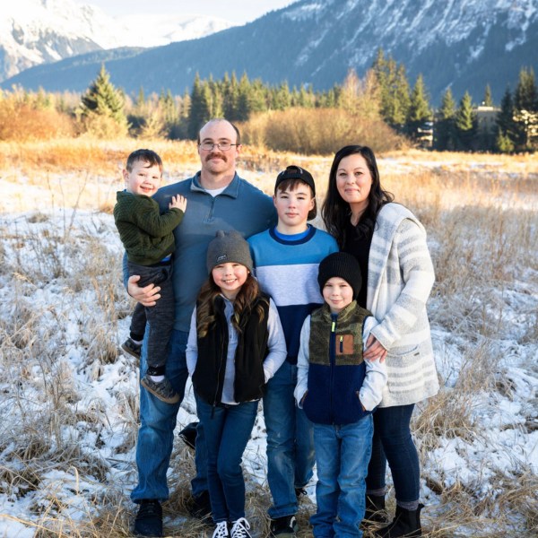 Family with three children posed in a snowy field with mountains and trees in the background.